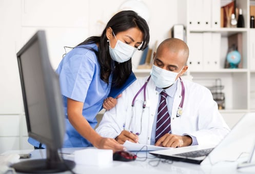 Doctor signing papers brought by female assisant in medical office