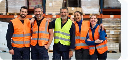 Group of five smiling workers in orange and yellow safety vests standing together in a warehouse